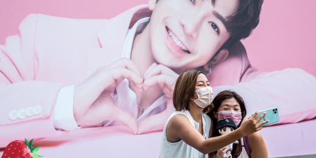 Dos mujeres se toman una selfie frente a una valla publicitaria que muestra una foto de Anson Lu, miembro del grupo de chicos Cantopop. "Espejo," En Hong Kong.