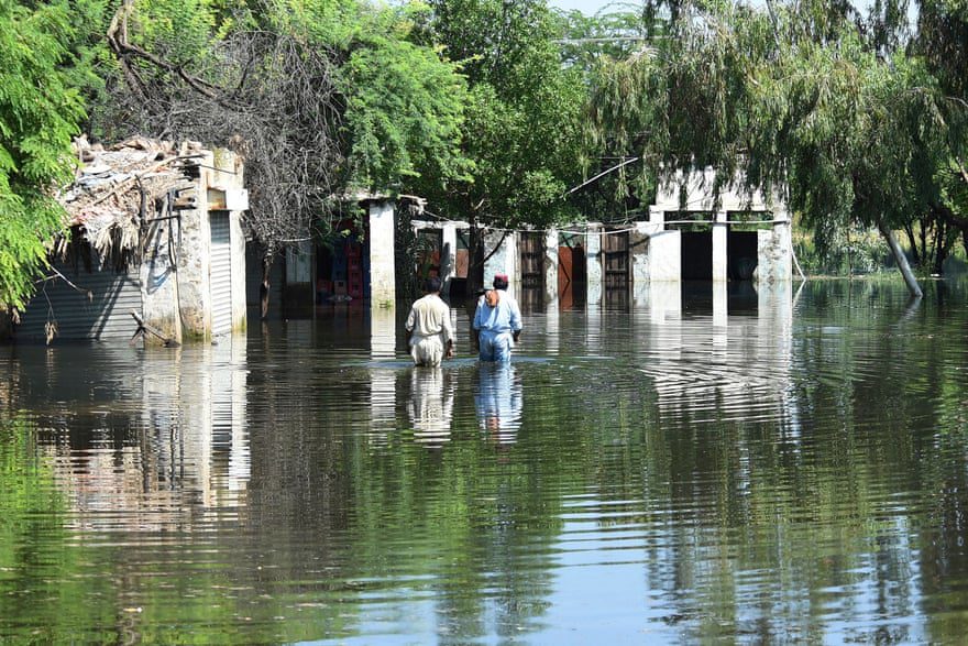 Los residentes caminan en las aguas de la inundación cerca de sus casas después de las fuertes lluvias del monzón.